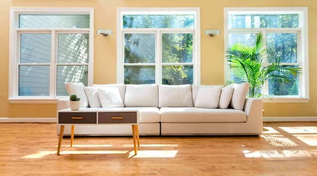 A white couch with beautiful windows and a nature view in a room with wood floors, sunny
