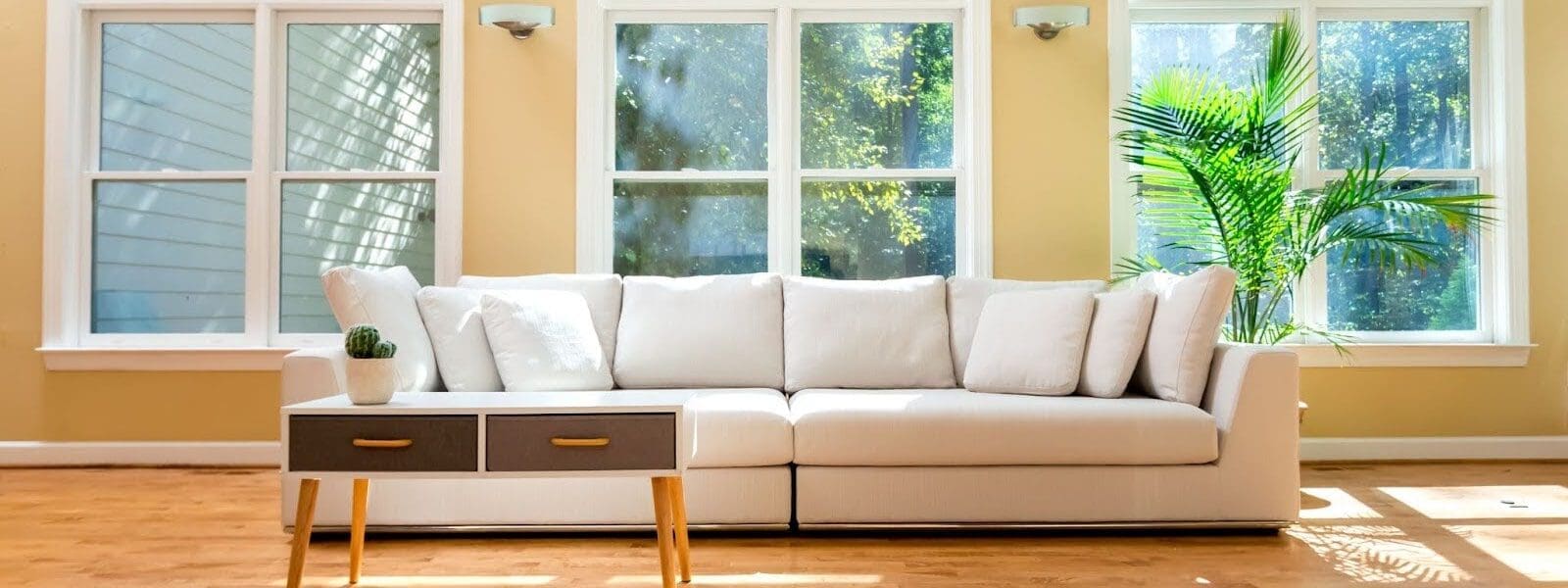 A white couch with beautiful windows and a nature view in a room with wood floors, sunny