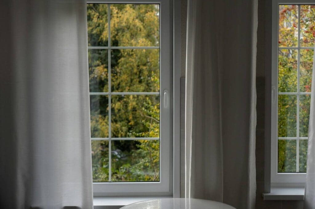 A pair of windows with curtains looking out to a green nature scene