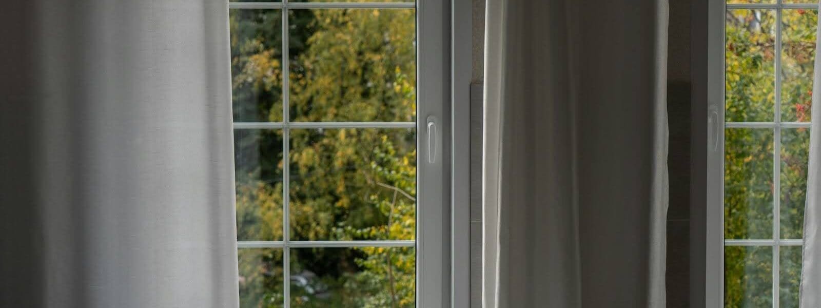 A pair of windows with curtains looking out to a green nature scene